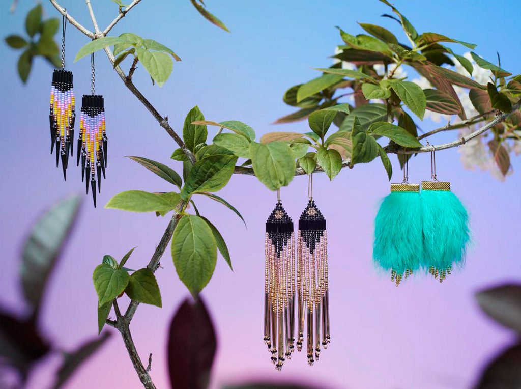 Tree branch with leaves, beaded and feather jewelry sit on branches. 