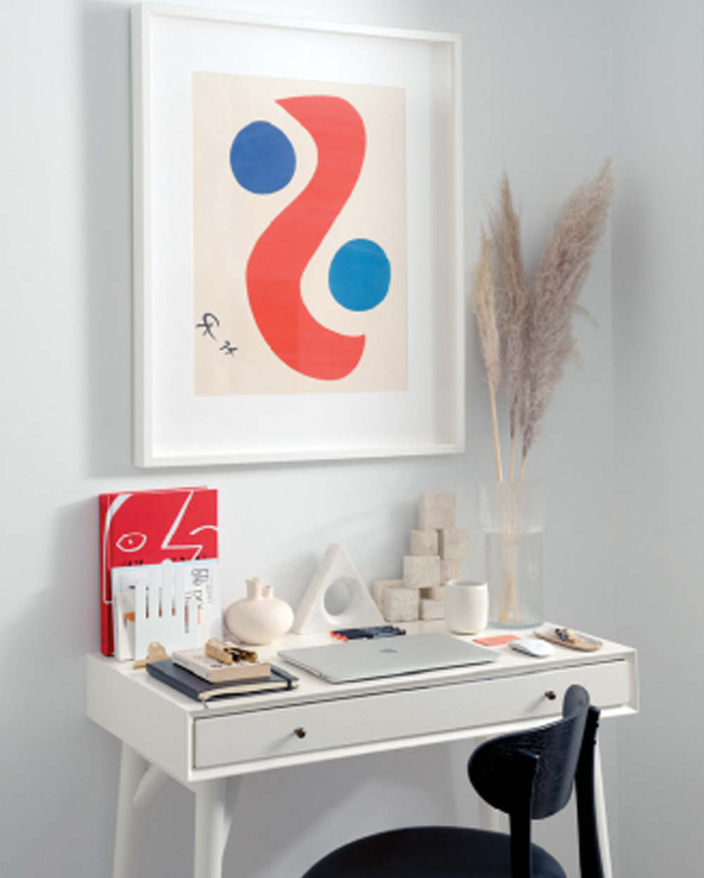 Desk set up with wall art, decorative pieces and chair in white office space.