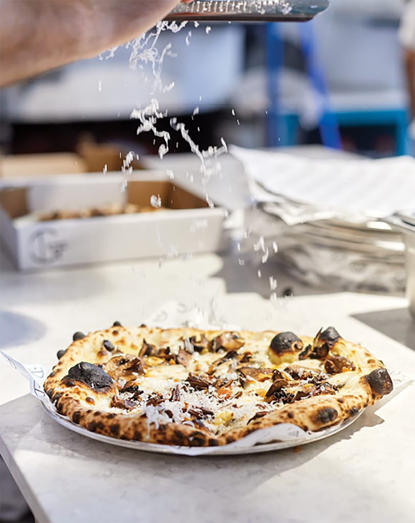 Cheese being grated on fresh pizza.
